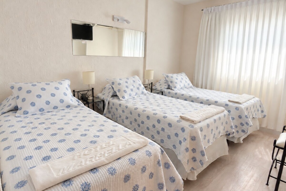 Habitación de hotel con dos camas, un espejo, un televisor de pantalla plana y una ventana con cortinas.