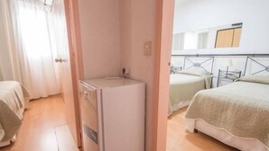 Habitación de hotel con distribución compacta, que incluye una cama, una kitchenette pequeña y una mesita de noche.