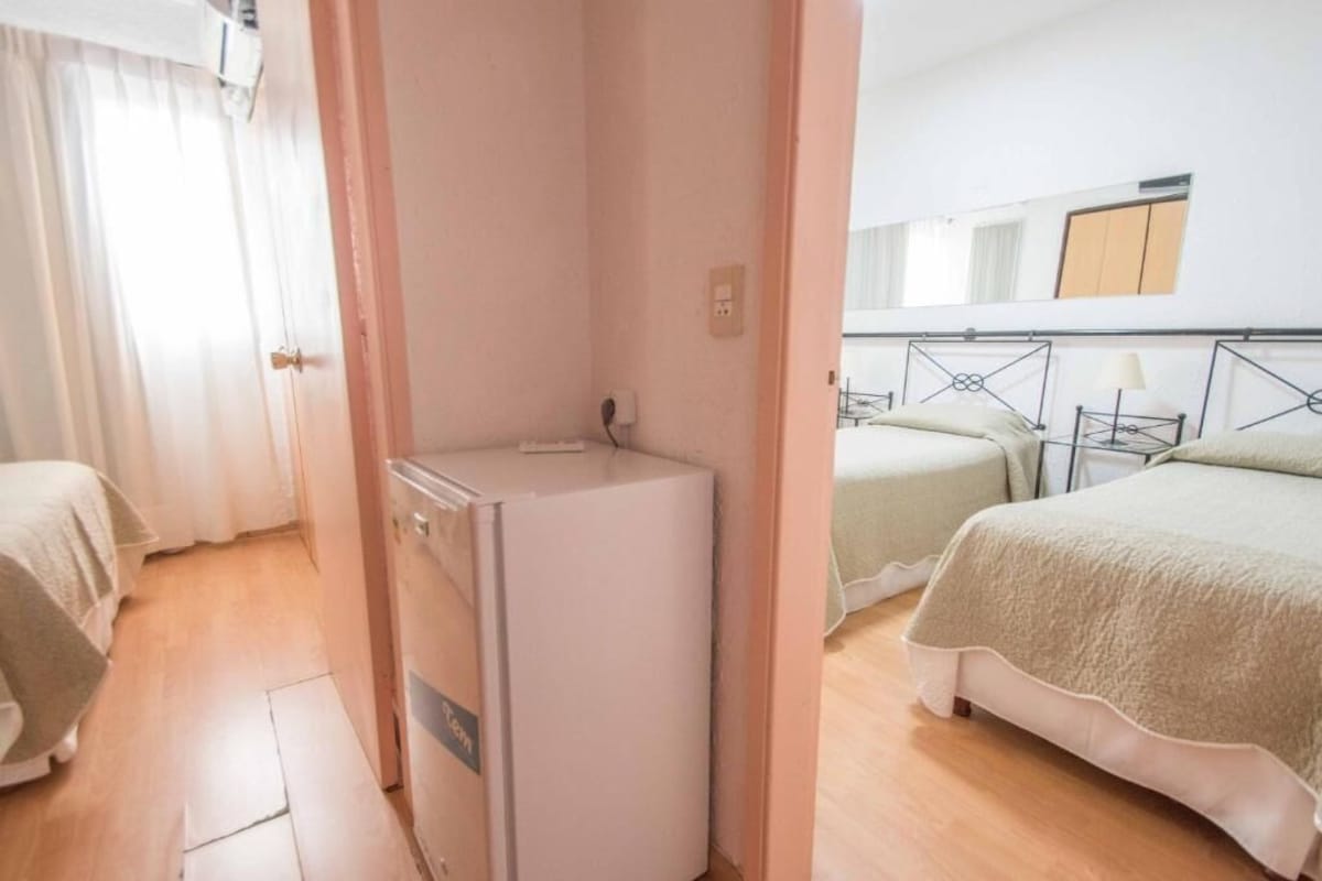 A hotel room with a compact layout, including a bed, a small kitchenette, and a bedside table.