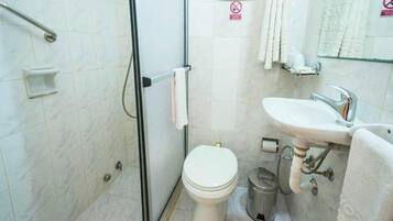 Casa de banho com chuveiro, sanita, lavatório e suporte para toalhas.