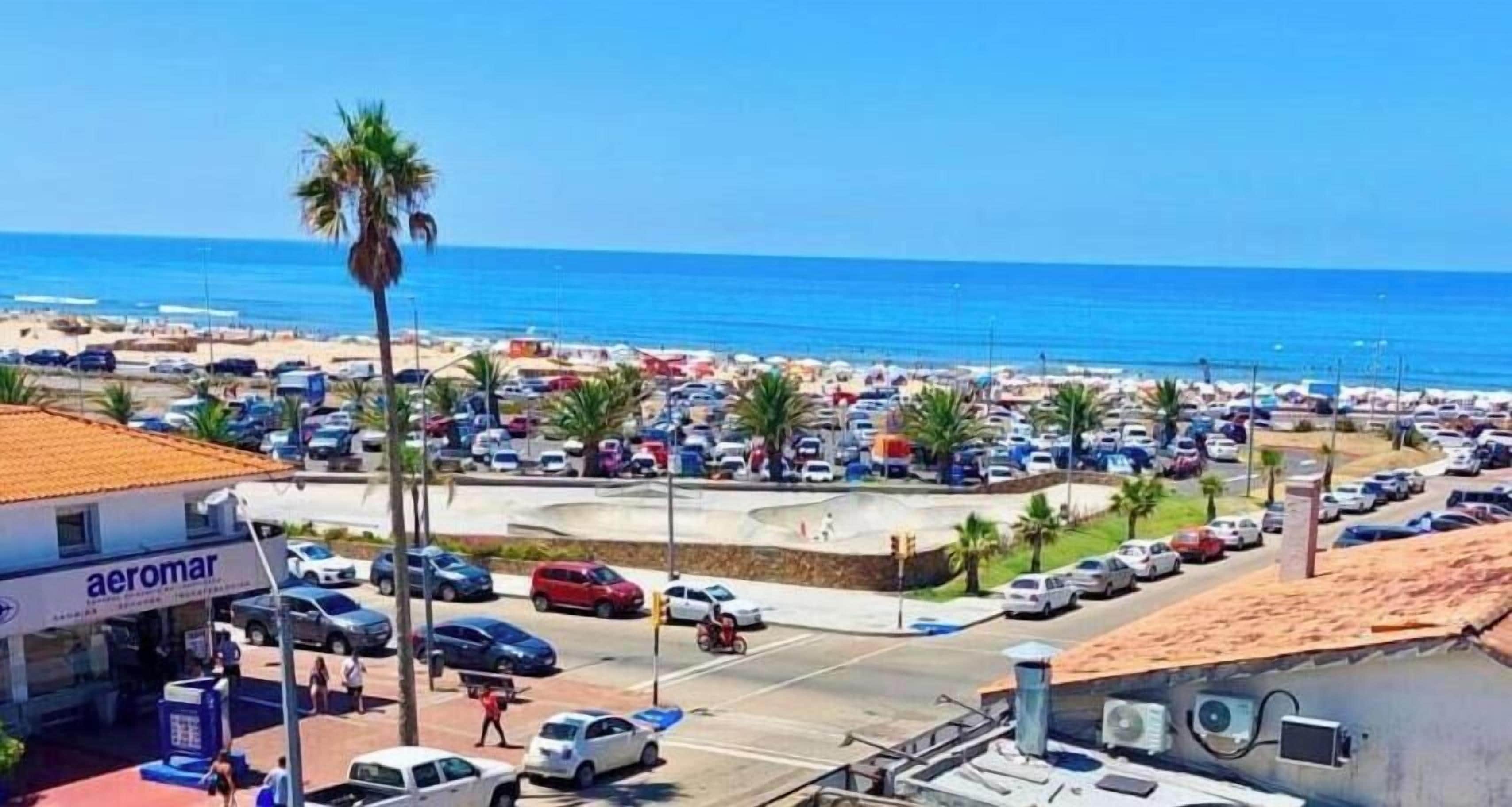 Un estacionamiento frente a la playa, con un edificio identificado como 'Aeromar', y vista al mar.