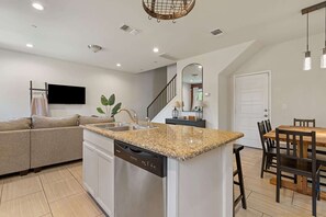 A modern kitchen with a granite countertop, built-in dishwasher, and a dining area with a wooden table and chairs.