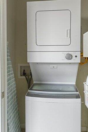 Un appareil compact combinant lave-linge et sèche-linge, installé dans une buanderie, avec un panneau de commande visible et une petite prise électrique.