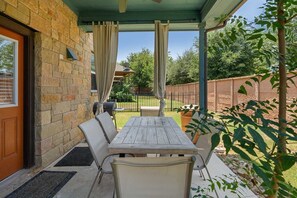 An outdoor patio with a table and chairs, a barbecue grill, and a covered area with curtains.