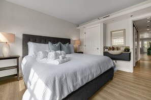 A modern hotel room with a large bed, two bedside tables, a nightstand, a bathroom with a sink and mirror, and a hallway leading to another room. - Walkable Downtown Asheville Retreat | Inc. Biltmore Pass & Parking (Asheville)