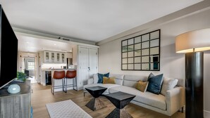 A modern living room with a sofa, coffee table, and chairs, a kitchen in the background, and a large mirror on the wall. - Walkable Downtown Asheville Retreat | Inc. Biltmore Pass & Dog Friendly (Asheville)