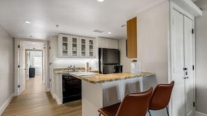 A modern kitchen with a granite countertop, stainless steel appliances, and a bar area with two leather chairs. - Walkable Downtown Asheville Retreat | Inc. Biltmore Pass & Dog Friendly (Asheville)