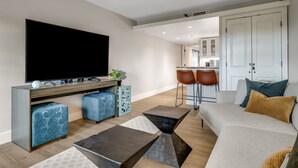 A modern living room with a flat-screen TV, a sofa, two ottomans, and a coffee table. - Walkable Downtown Asheville Retreat | Inc. Biltmore Pass & Dog Friendly (Asheville)