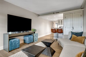 Ett modernt vardagsrum med en platt-TV, en soffa, två sittpuffar och ett soffbord.