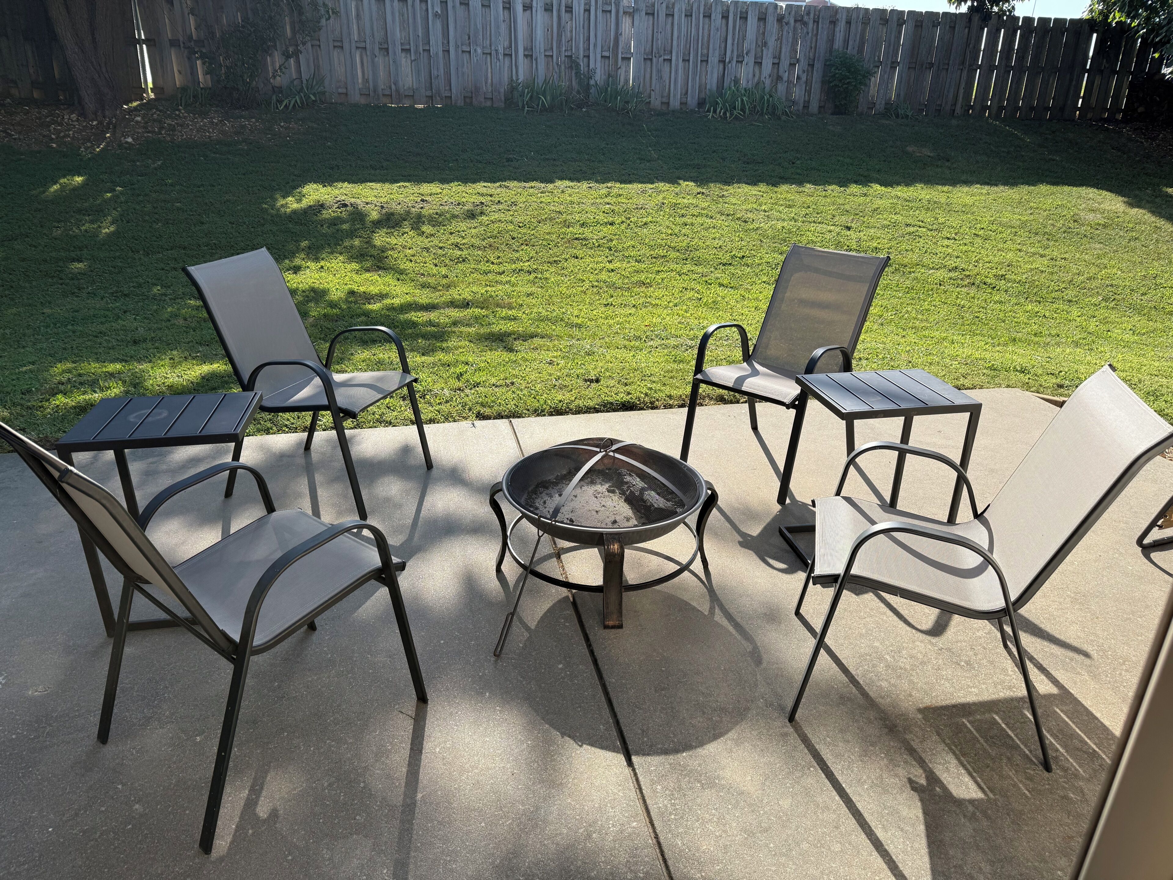 An outdoor patio with four metal chairs and a fire pit.