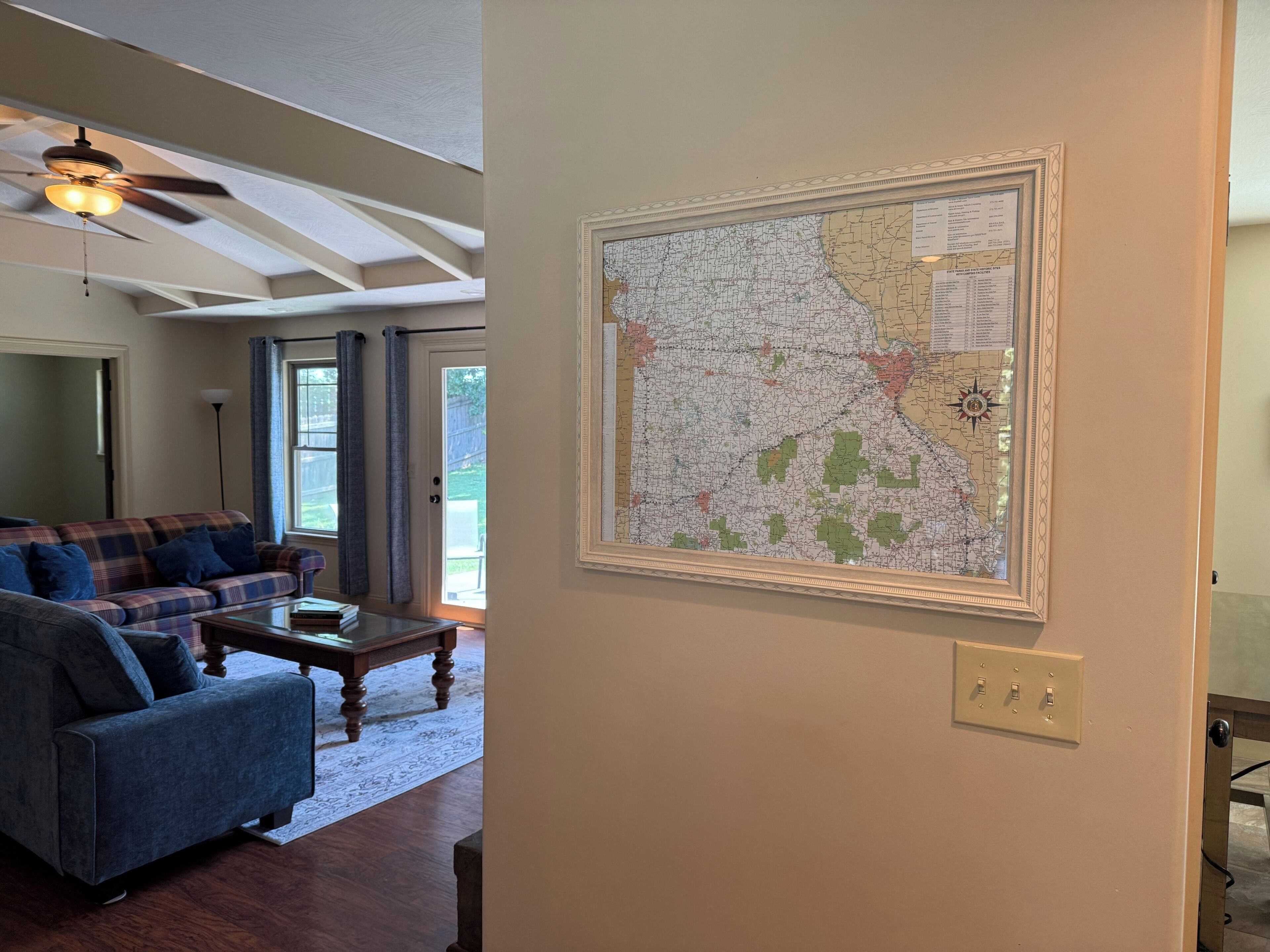 A living room with a large wall map, a ceiling fan, and a plaid sofa.