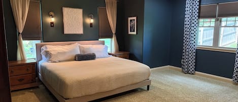 Quarto com cama, mesas de cabeceira, ventilador de teto e janela com cortinas.