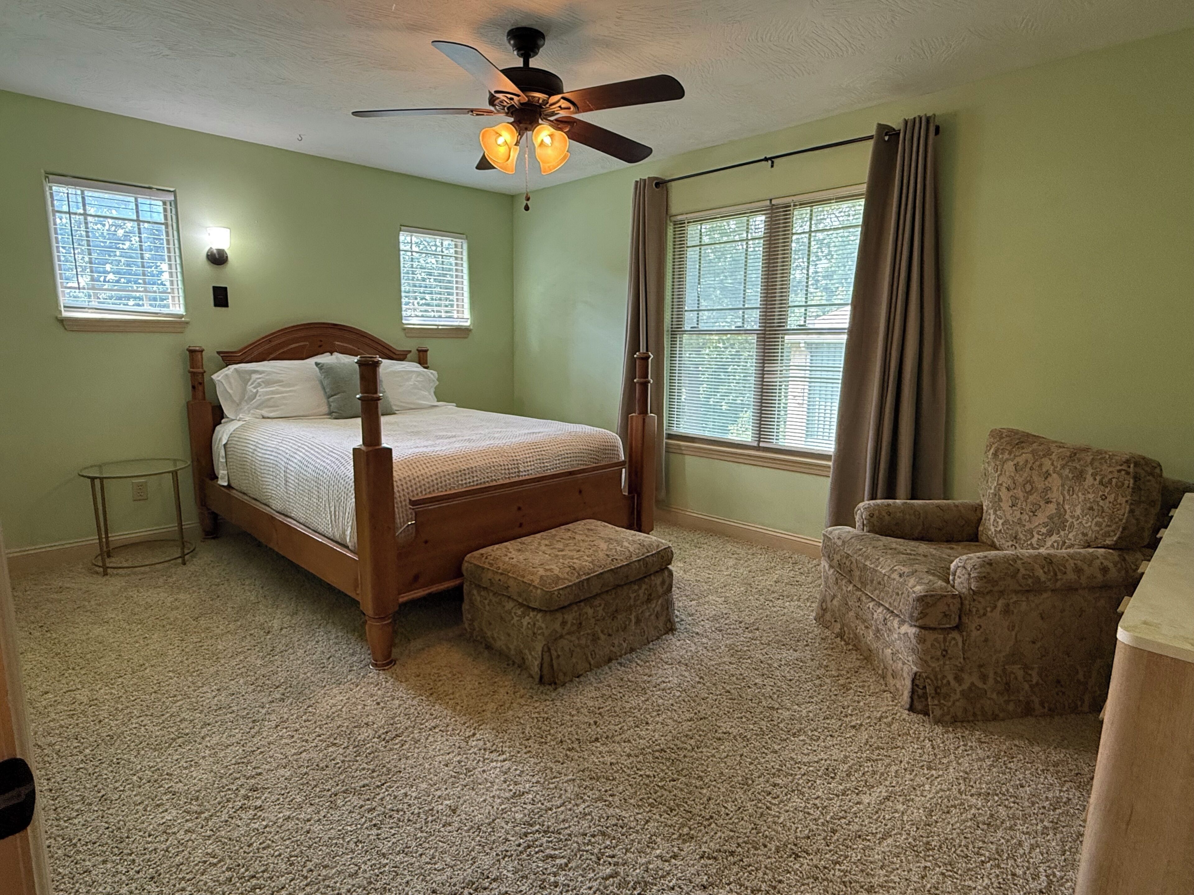 A bedroom with a four-poster bed, a ceiling fan, a chair, and a window with blinds.