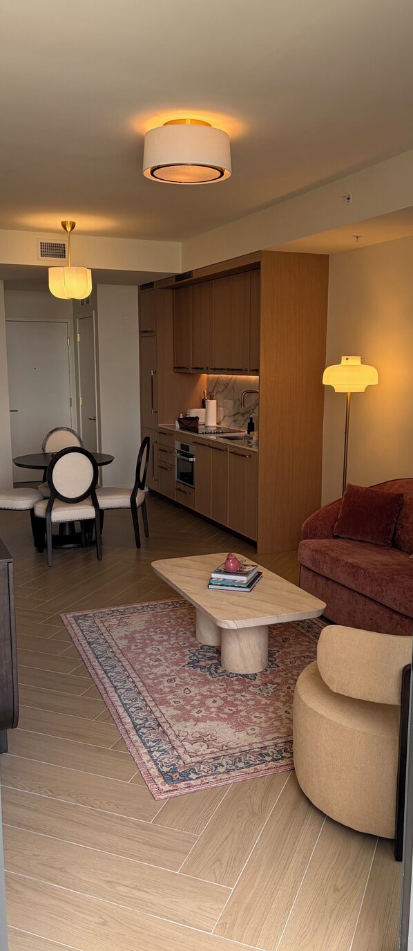 A modern living room with a sofa, a coffee table, a dining area with chairs, a kitchen with wooden cabinets, and a patterned rug on the floor. - Nomad Wynwood - Boutique luxury 1 bedroom+Den+2B (Miami)