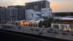 A modern building with a geometric facade, a parking lot with several cars, and a street view with a restaurant. - Nomad Wynwood - Boutique luxury 1 bedroom+Den+2B (Miami)