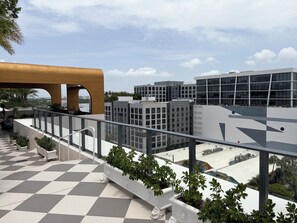 En tagterrasse med skakternet gulv, plantekasser og udsigt til moderne bygninger.