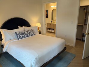 A neatly made bed with white linens and a floral pillow, a bedside lamp, and a view into a bathroom with a mirror and towel rack. - Nomad Wynwood - Boutique luxury 1 bedroom+Den+2B (Miami)