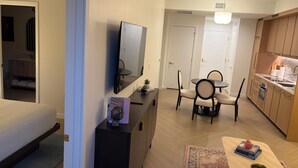A modern living room with a flat-screen TV, a dining table with chairs, a kitchen area with wooden cabinets, and a small rug on the floor. - Nomad Wynwood - Boutique luxury 1 bedroom+Den+2B (Miami)
