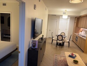 A modern living room with a flat-screen TV, a dining table with chairs, a kitchen area with wooden cabinets, and a small rug on the floor. - Nomad Wynwood - Boutique luxury 1 bedroom+Den+2B (Miami)