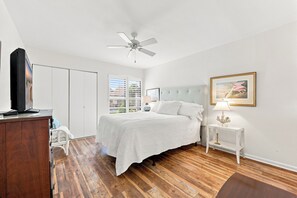 Ein Schlafzimmer mit einem Bett, einem Deckenventilator, einem Nachttisch mit Lampe, einem gerahmten Bild an der Wand und einem Kleiderschrank.