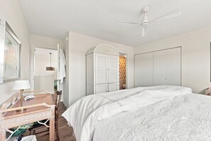 Ein Schlafzimmer mit Bett, Kleiderschrank, Spiegel und Deckenventilator.
