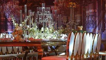 A formal dining table with a floral centerpiece, surrounded by white chairs with gold accents.