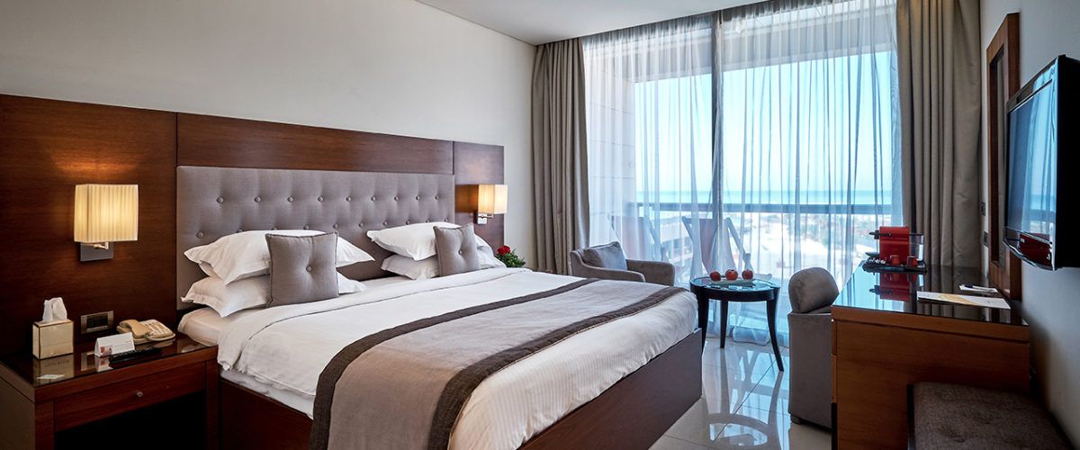 A hotel room with a large bed, a desk, a chair, a TV, and a view of the outdoors.