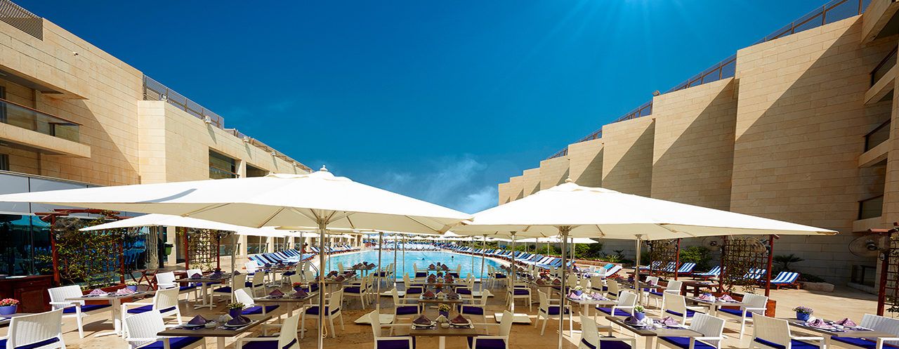 A poolside area with sun loungers and umbrellas, a pool, and a building with a modern design.
