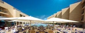 Un espace aménagé au bord de la piscine, avec des chaises longues et des parasols, une piscine, et un bâtiment au design moderne.