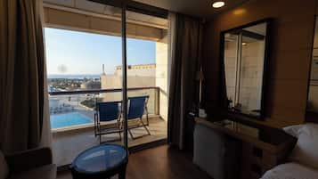 A hotel room with a balcony, a small table, a chair, a bed, and a large mirror.