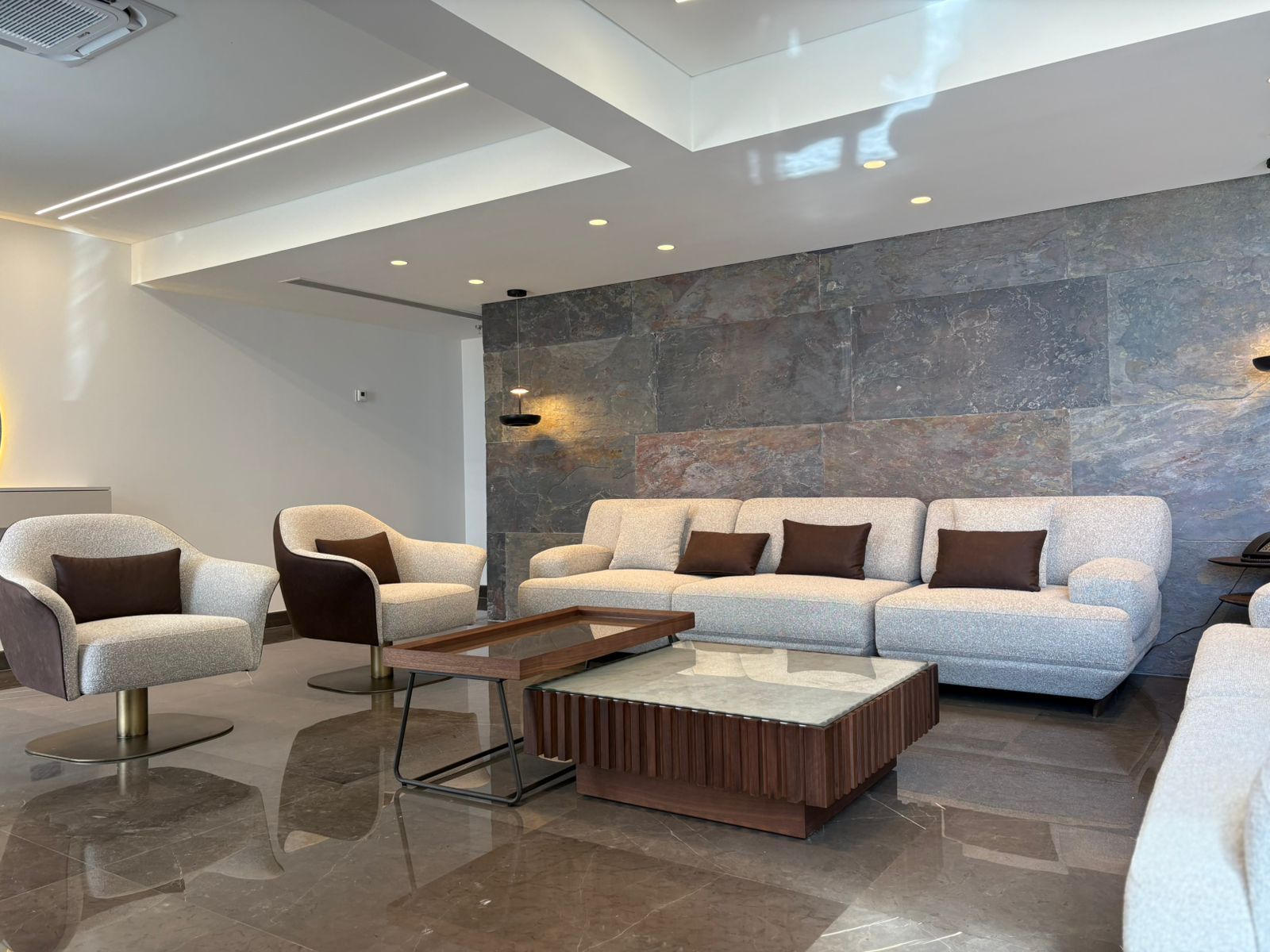 Un interior moderno con un conjunto de sofás, dos sillones, una mesa de centro y una pared de acento de piedra.