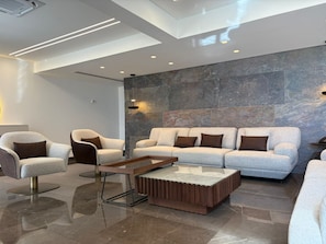 Un intérieur moderne comprenant un ensemble de canapés, deux fauteuils, une table basse et un mur d’accent en pierre.