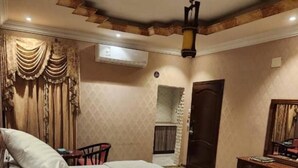 A hotel room with a bed, a desk, a chair, an air conditioning unit, and a patterned carpet.