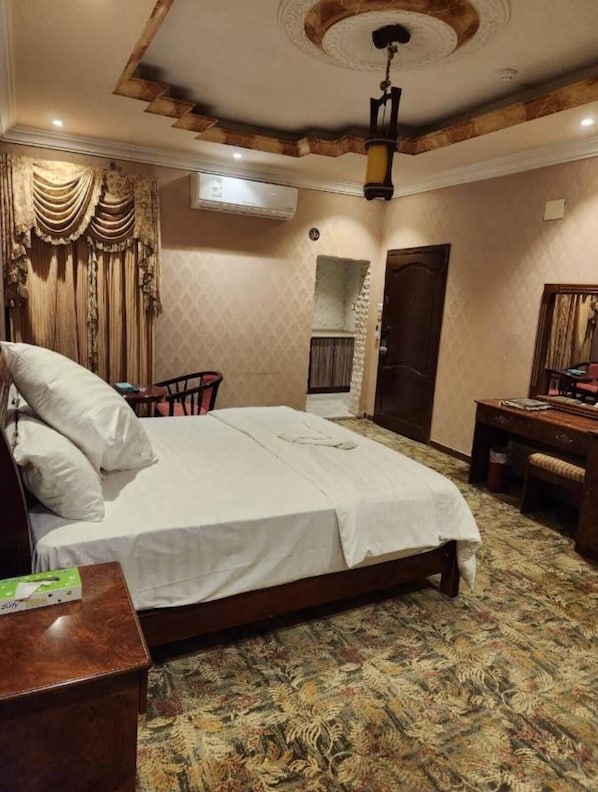 Habitación de hotel con cama, escritorio, silla, equipo de aire acondicionado y alfombra estampada.