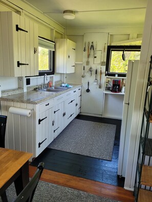 A compact kitchen with white cabinets, a granite countertop, a sink, and a window with a view of greenery.