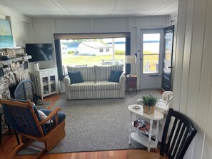 Una sala de estar con un sofá, un sillón mecedora, un televisor y vistas al exterior.