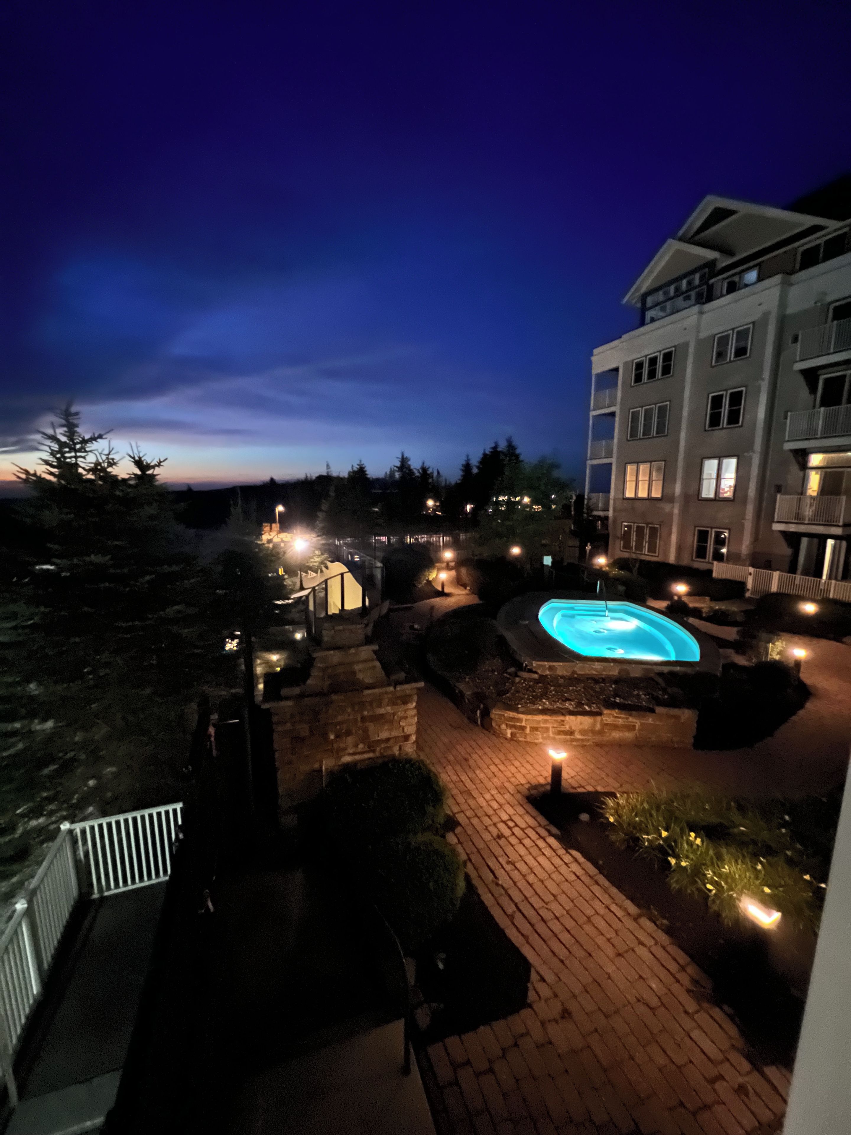 A nighttime view of a hotel courtyard with a swimming pool, stone pathways, and a building with multiple windows.