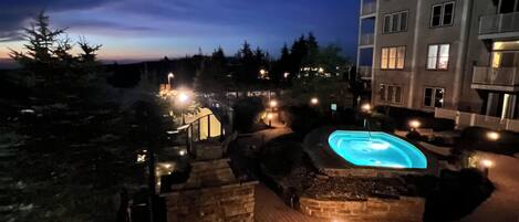 A nighttime view of a hotel courtyard with a swimming pool, stone pathways, and a building with multiple windows.