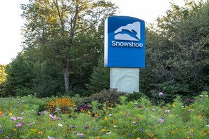 A sign for Snowshoe with a mountain silhouette, surrounded by a field of wildflowers and trees. - Newest property in our portfolio! Discounted! Snowshoe Village Ski-in - Ski-out Condo w/ Underground Parking & Community Hot Tub (Snowshoe)