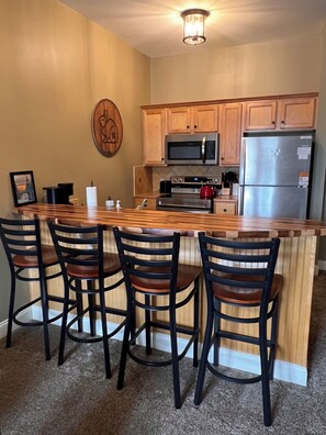 A kitchen with a wooden island, bar stools, a microwave, oven, and refrigerator. - Newest property in our portfolio! Discounted! Snowshoe Village Ski-in - Ski-out Condo w/ Underground Parking & Community Hot Tub (Snowshoe)