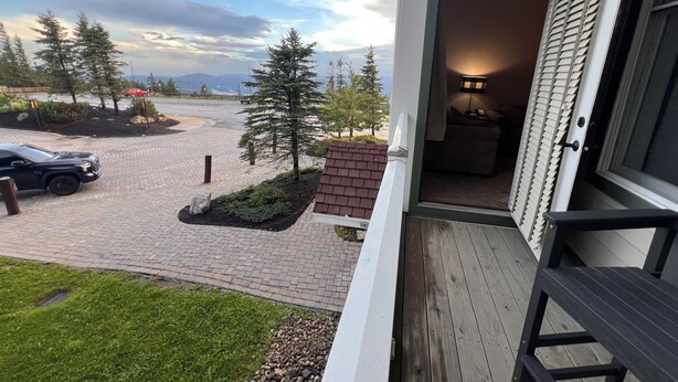 En bostadsfastighet med en asfalterad uppfart, en gräsmatta, ett trädäck och utsikt över en väg och träd.