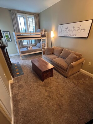 A room with a bunk bed, a sofa, a small wooden table, and a wall-mounted lamp. - Snowshoe Village Ski-in - Ski-out Condo w/ Hot Tub (1 Br / 1 Ba) (Snowshoe)
