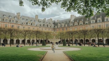 A courtyard with a central fountain, surrounded by a symmetrical building with multiple windows and a paved walkway.