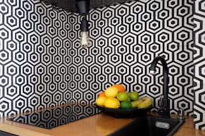 A kitchen with a black and white hexagonal tile backsplash, a black faucet, and a bowl of fruit on the counter. - Cozy Studio for 2 in Le Marais - Central Paris (Paris)