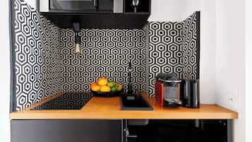 A kitchen with a black and white geometric backsplash, a wooden countertop, a sink, a fruit bowl, and a microwave.