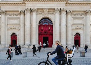 Ein historisches Gebäude mit klassischer Architektur, das große Säulen, kunstvolle Portale und ein zentrales Buntglasfenster zeigt.