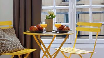 A yellow table with croissants, orange juice, and a flower vase by a window.