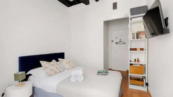 A bedroom with a bed, a nightstand, a TV mounted on the wall, and a wardrobe.