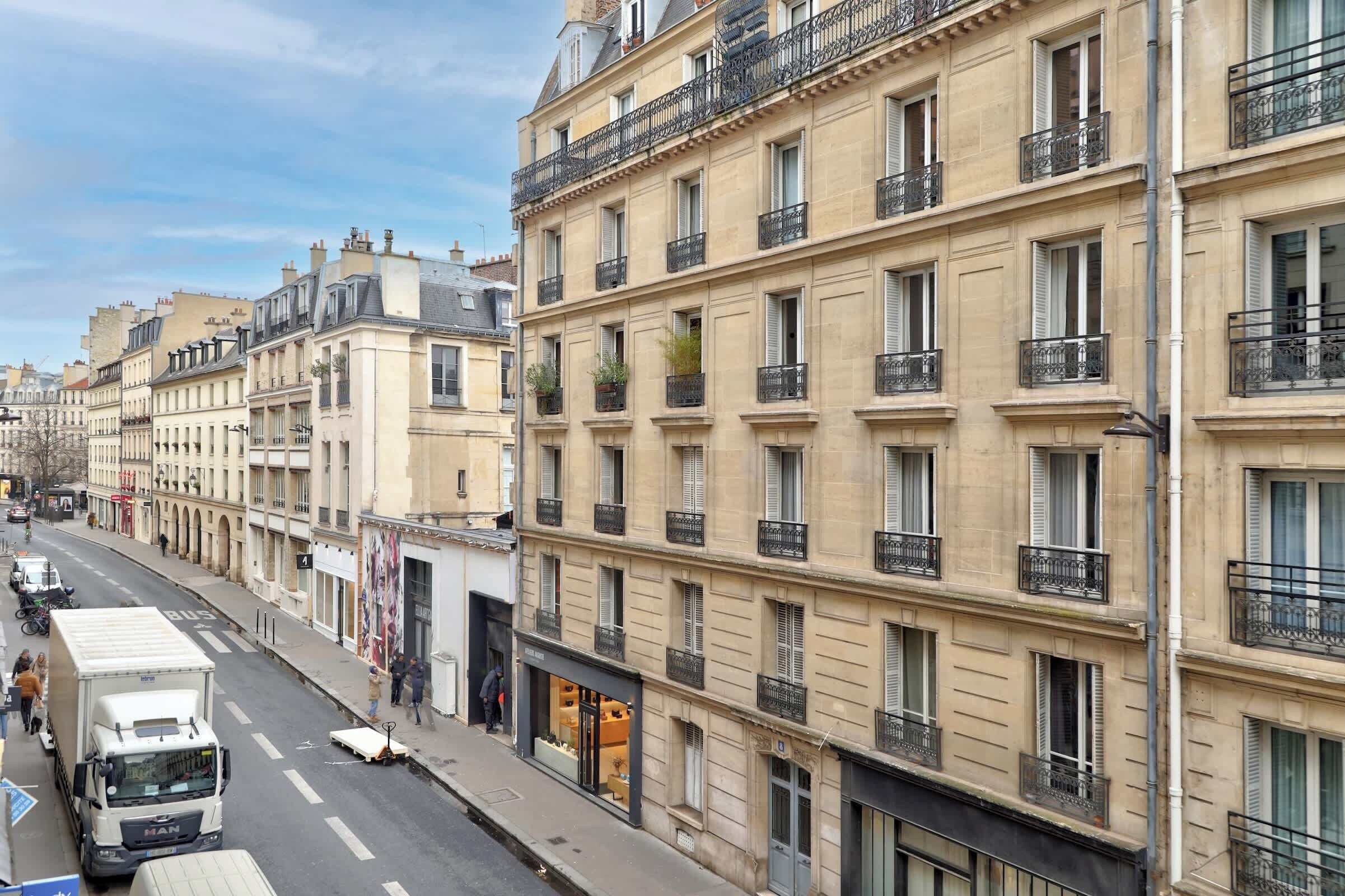 Vista de una calle con un edificio parisino de varios pisos, balcones y un escaparate.