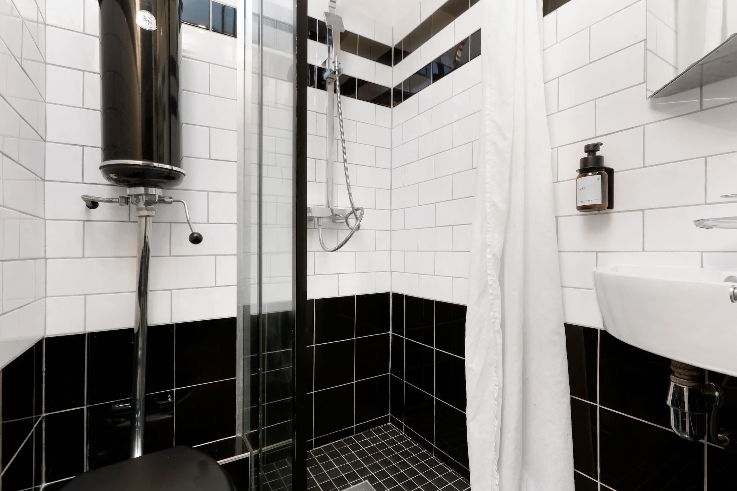 A modern bathroom with a black and white tiled design, a glass shower enclosure, and a white sink.
